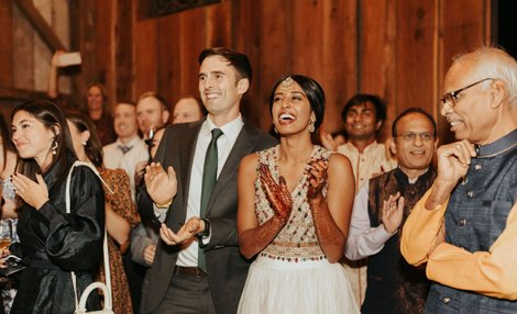 mixed race wedding couple watching friends dance at their western - hindu wedding. american and indian wedding couple