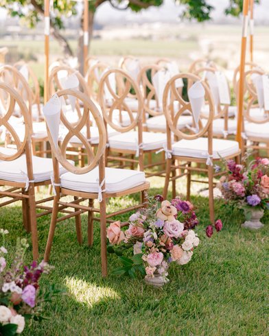 light wooden ceremony chairs with cones for flower petals. Ceremony aisle lined with flowers. 
