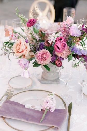 bright colorful wedding centerpiece with mauve, peach, purple flowers. flower on napkin with napkin wrapped around charger