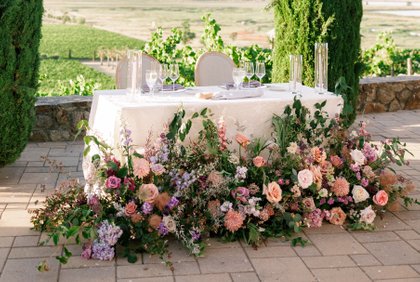 sweetheart table flower decorations. flowers in ground arrangement in front of sweetheart table. purple, mauve, peach floral