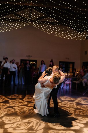 First dance of wedding couple with rose pattern lights on dance floor with twinkle lights in canopy above dance floor. 